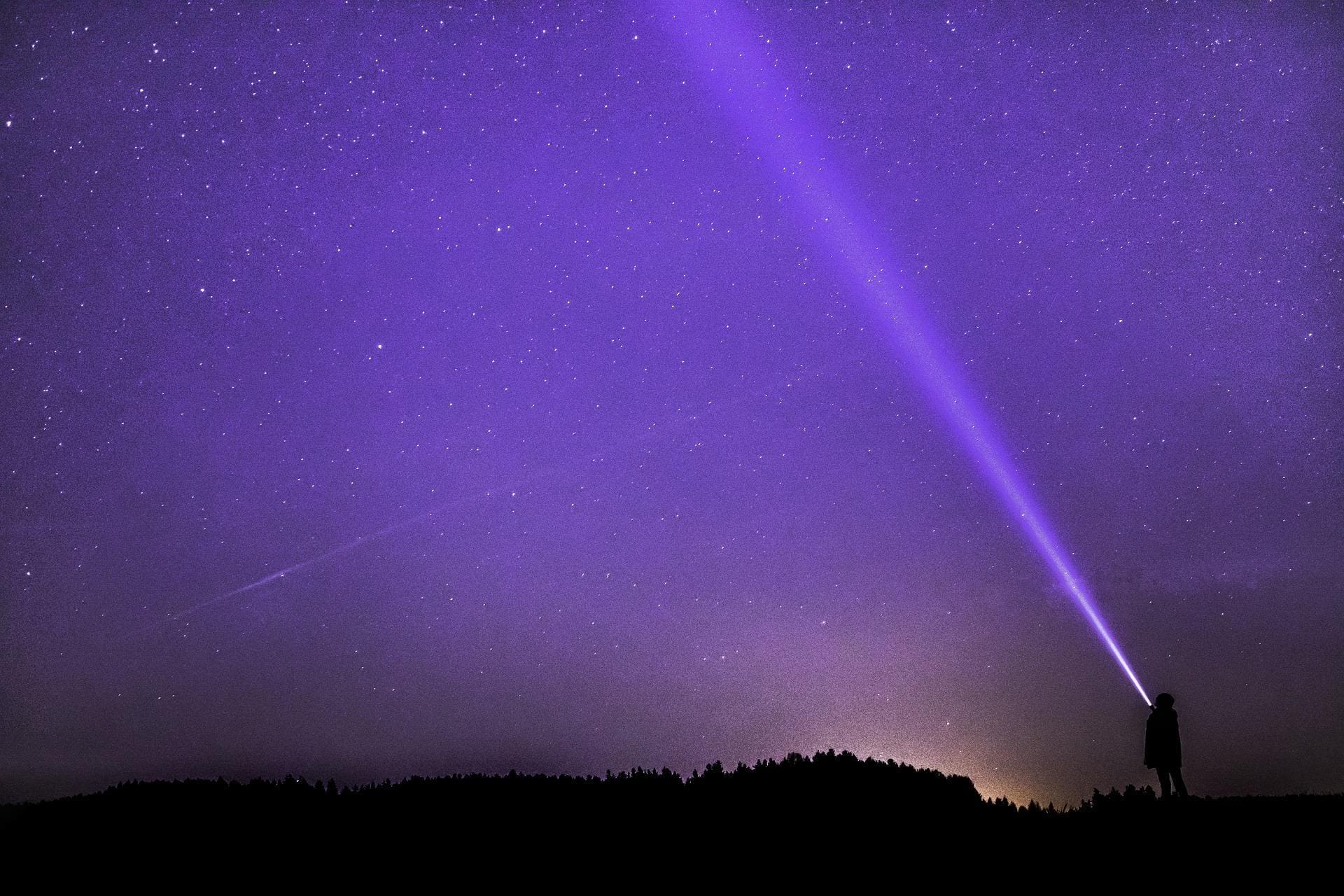 Photograph of a person illuminating the starry sky with a flashlight.