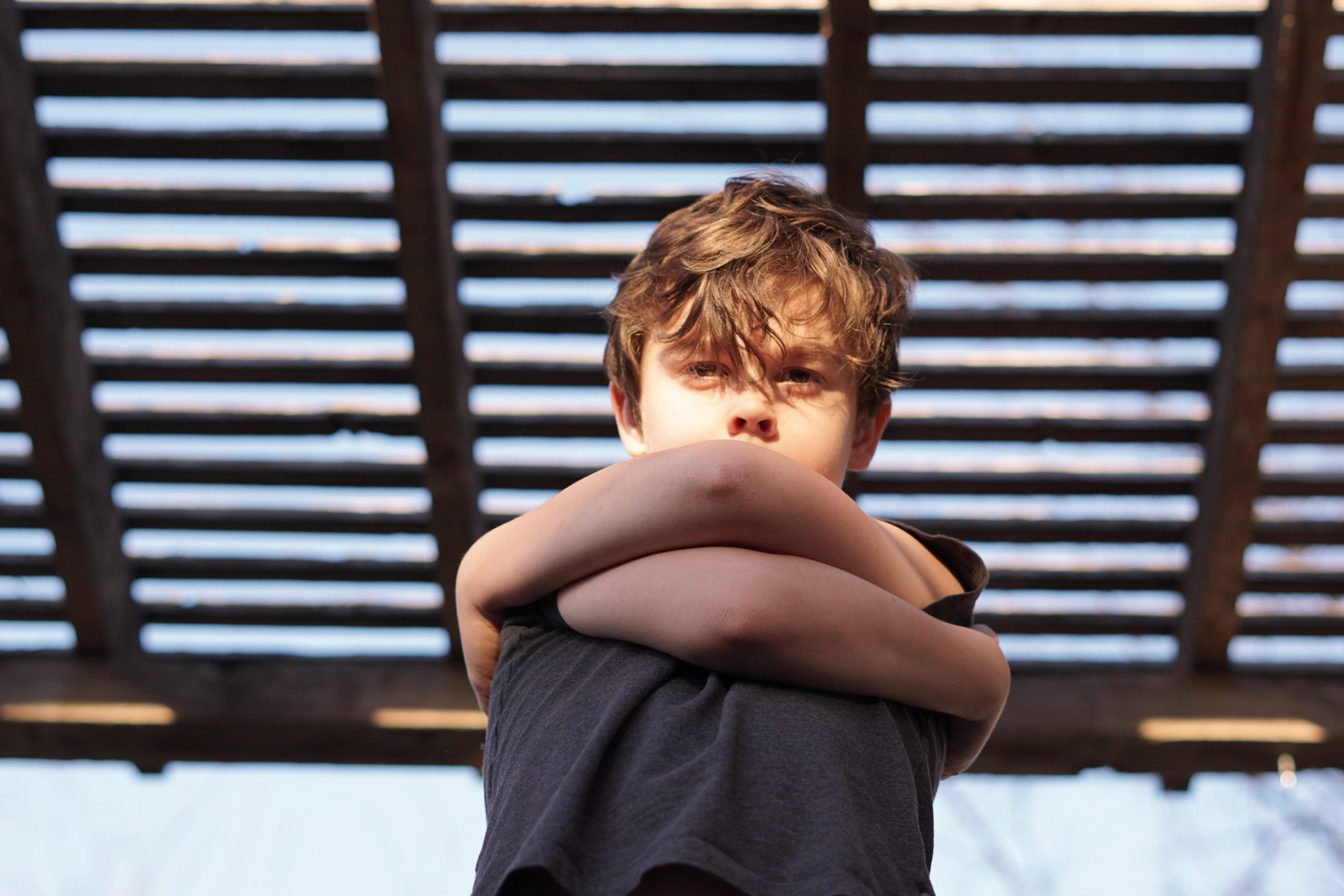 Photograph of young boy hugging himself.