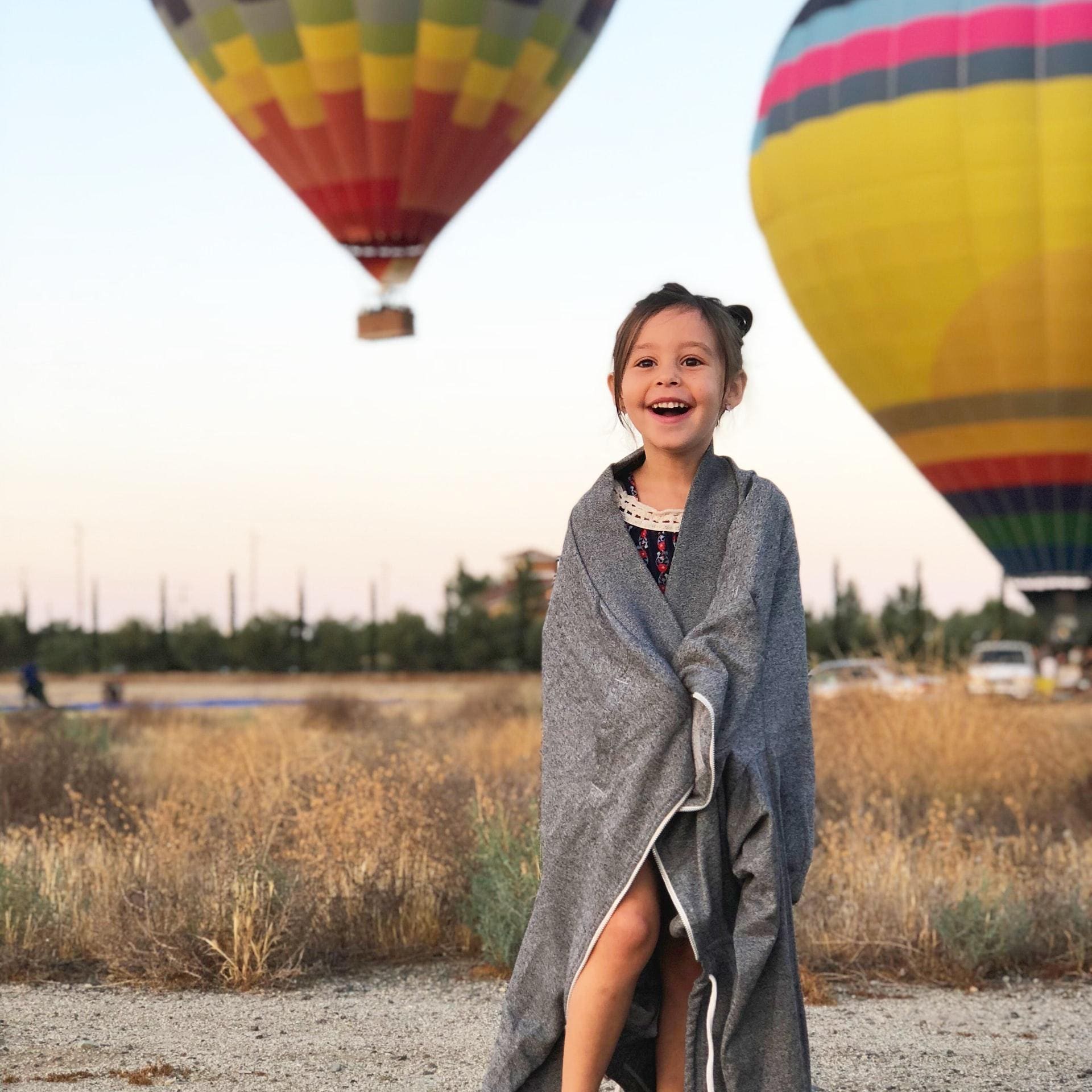 Photograph of a happy, smilling child (girl). In the background are two hot air balloons raising up.