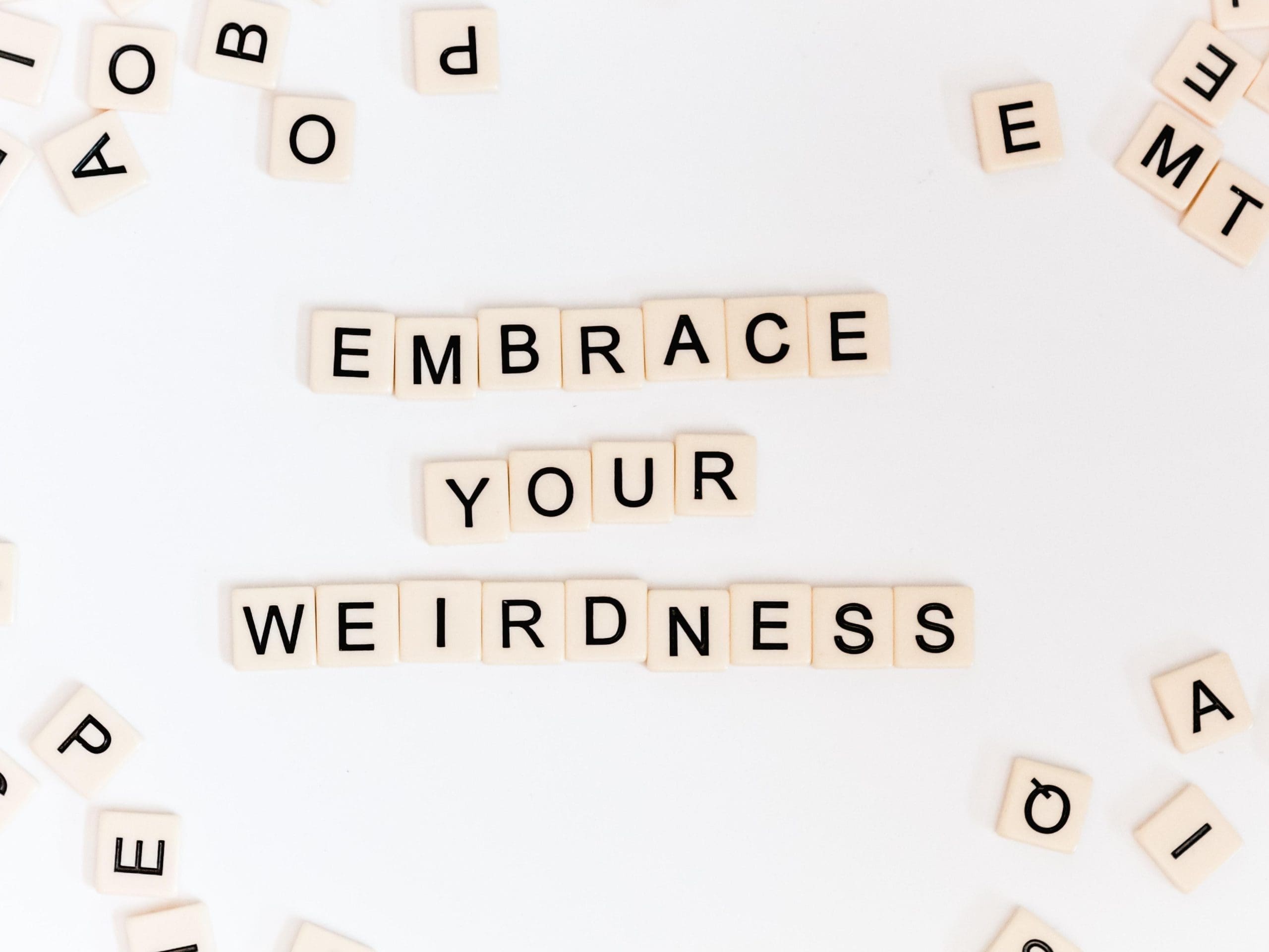 Digital art of scrabble tiles. Some of them are forming the sentence: "embrace your weirdness".