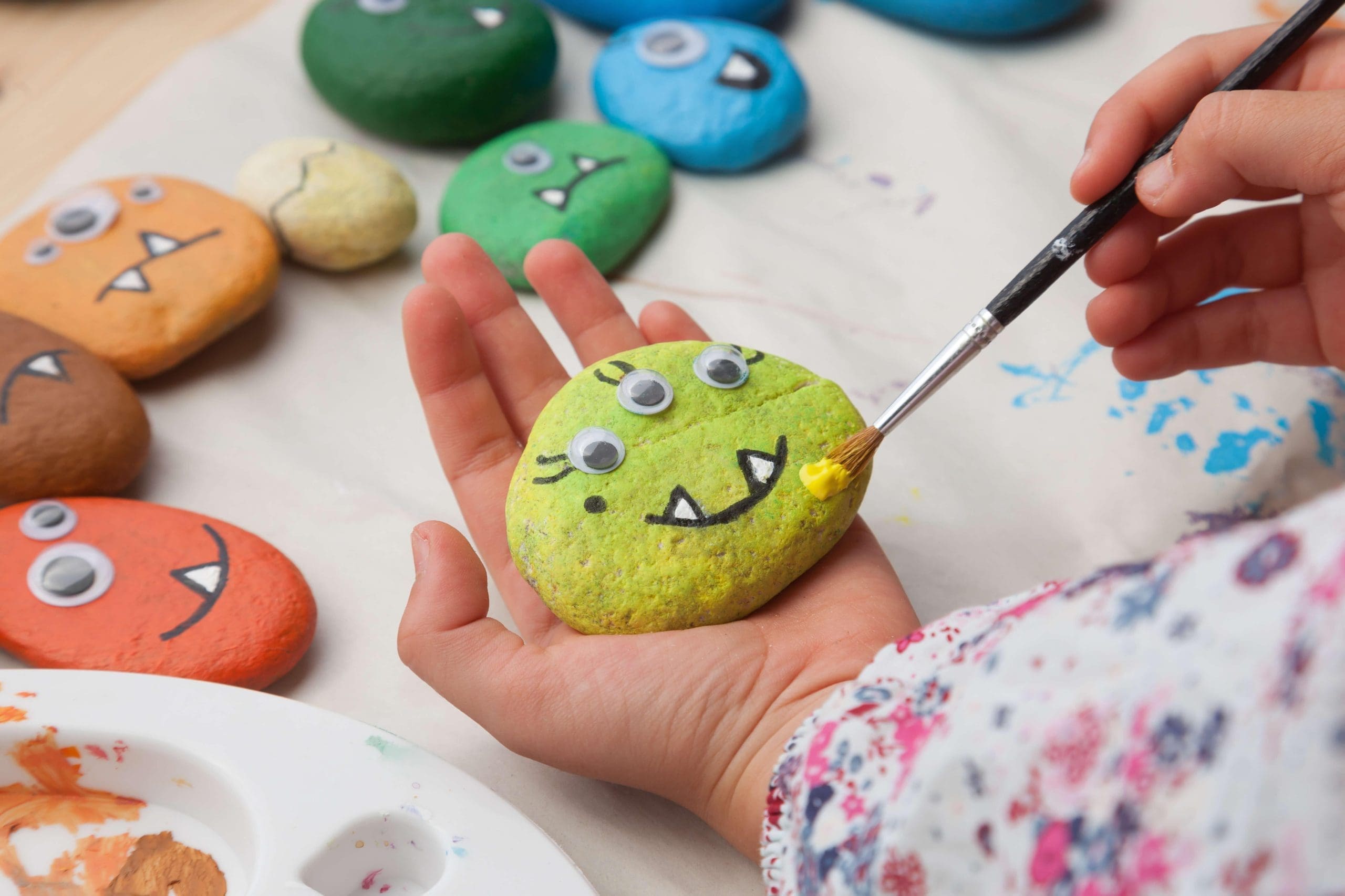 Photograph of a child's hand holding a stone painted as a monster. 