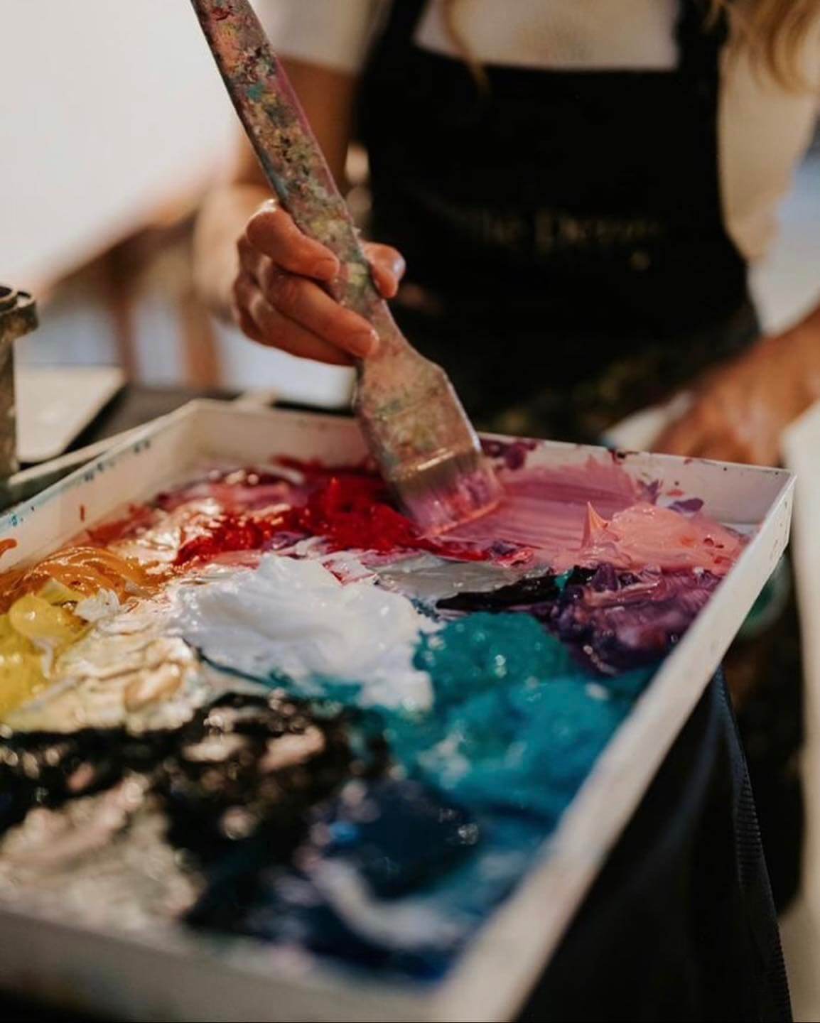 Photograph of Giselle Denis' creative process. She uses a big, wooden brush to mix the paint, so she can reach the hue she needs for her painting.