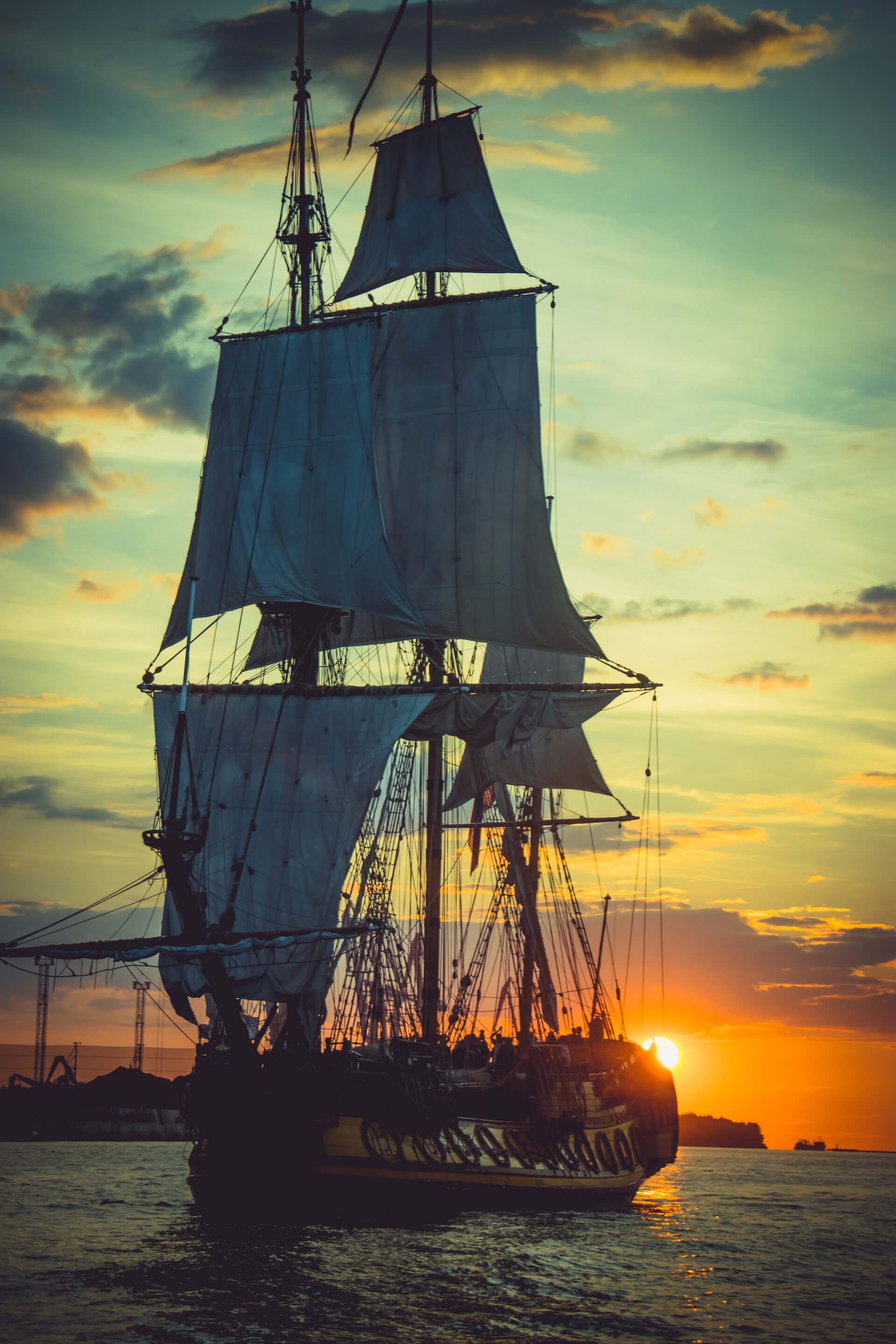 Photograph of a pirate ship on the water, while in the background, the sun is setting.