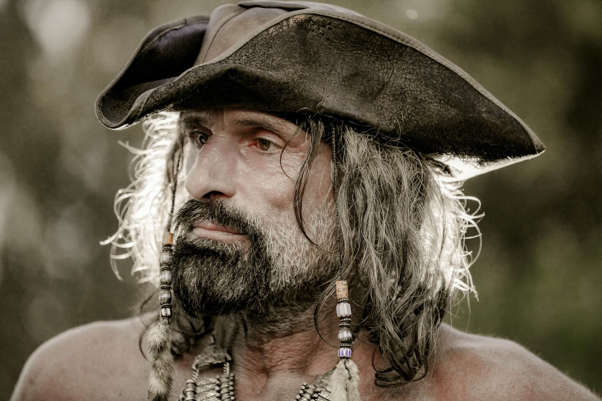 A close-up photograph of a pirate man wearing a pirate hat. He has long hair and a beard. He looks serious and concerned, away from the camera.