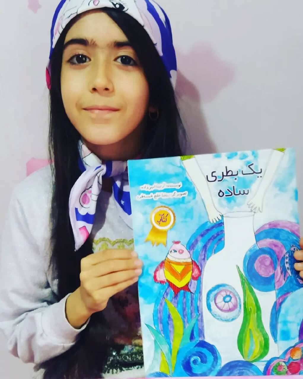 Photograph of Ronia Khalaj holding proudly in her hands one of her published children's books.