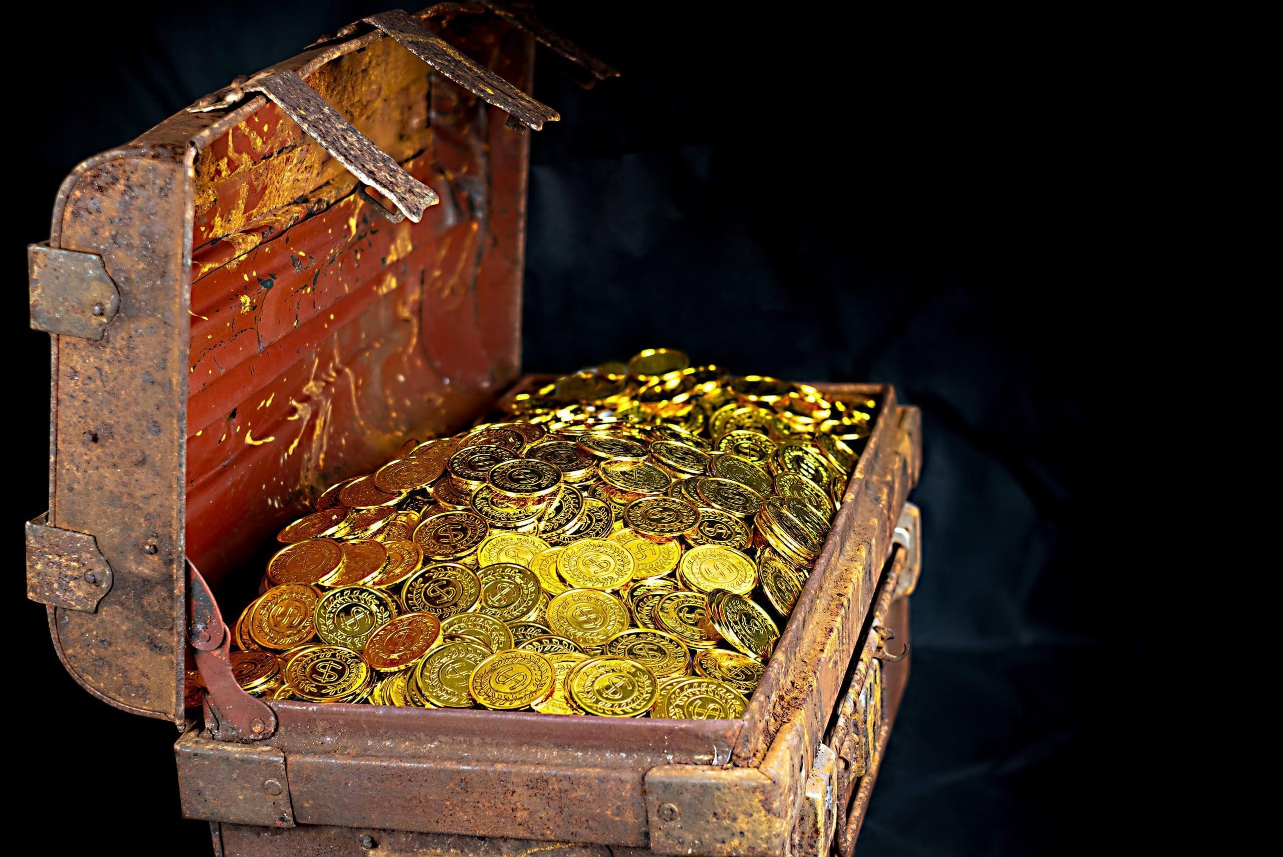 Photograph of an old, wooden chest filled with gold coins.