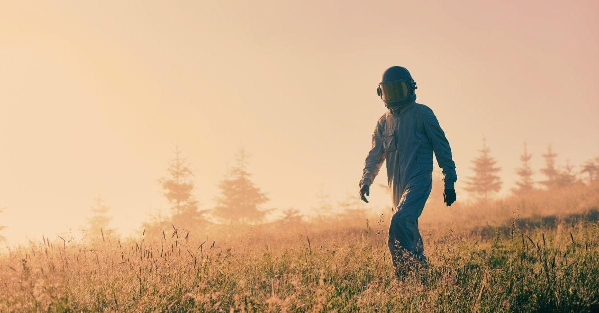 Cosmonaut in space suit walking down the meadow with lush grass. 